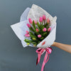 Bouquet of pink tulips wrapped in white paper with a pink ribbon against a gray background