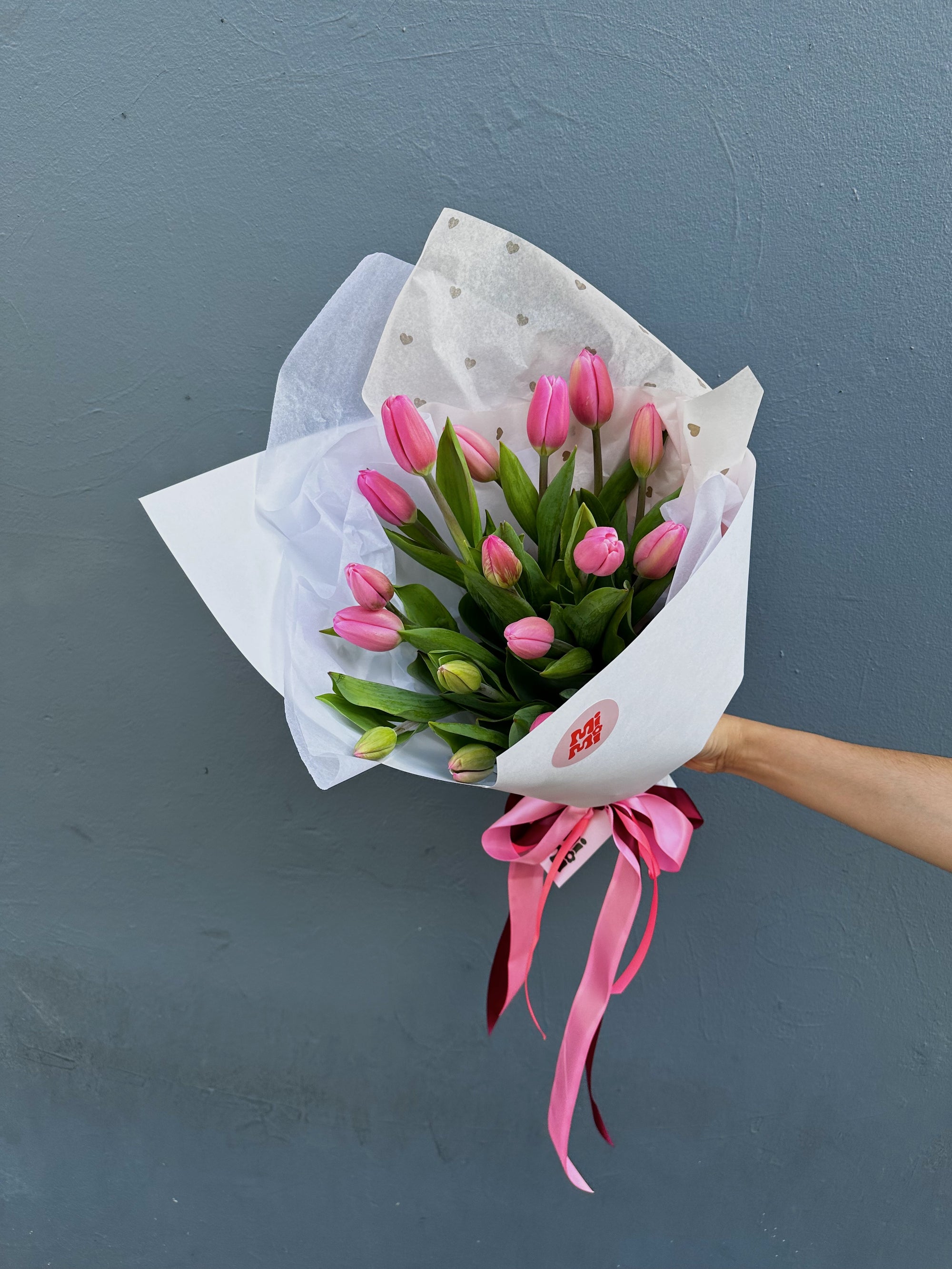 Bouquet of pink tulips wrapped in white paper with a pink ribbon against a gray background