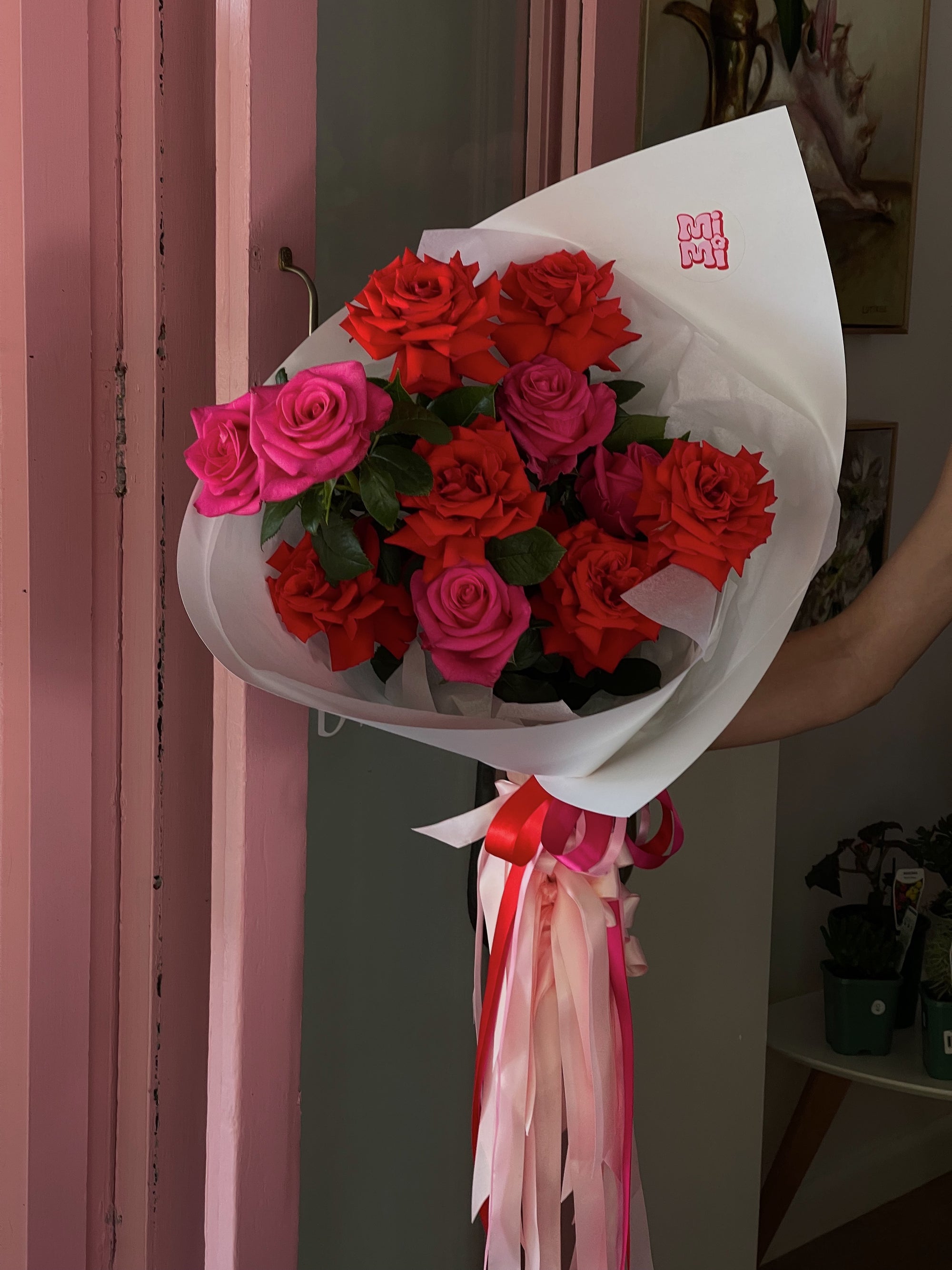 A bouquet of mixed roses with red and pink flowers, wrapped in white paper with decorative elements and ribbons.